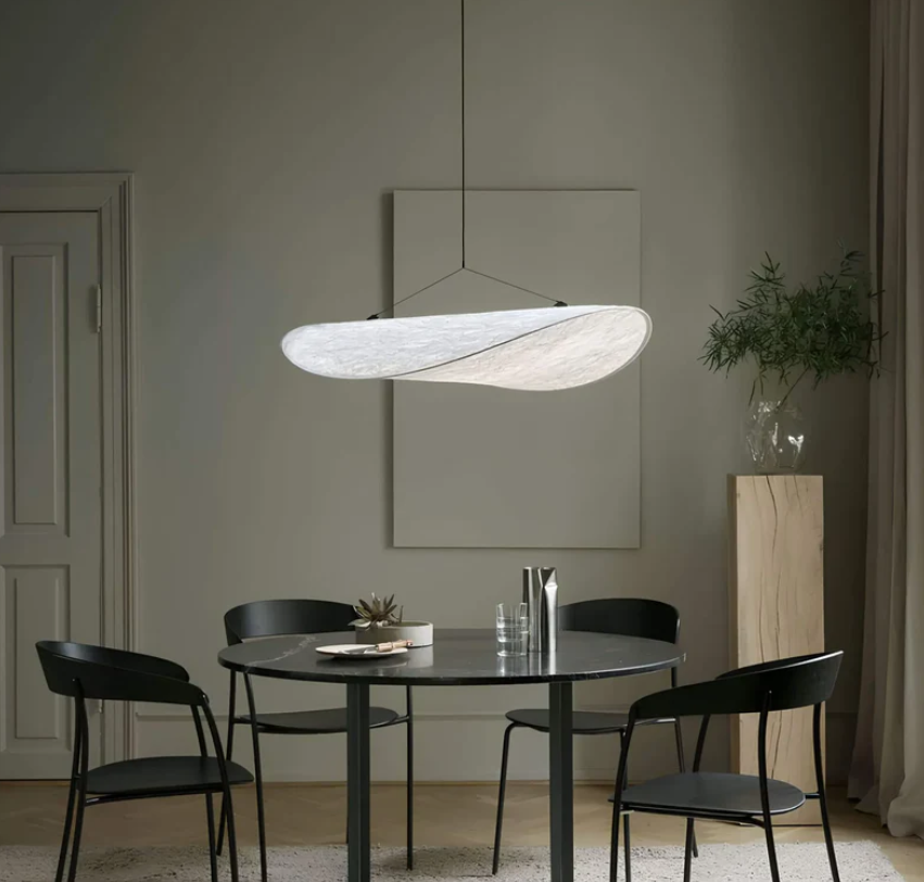 Moderne spisestue med sort rundt bord, fire sorte stole og elegant hvid pendellampe. Minimalistisk indretning med grøn plante i hjørnet.