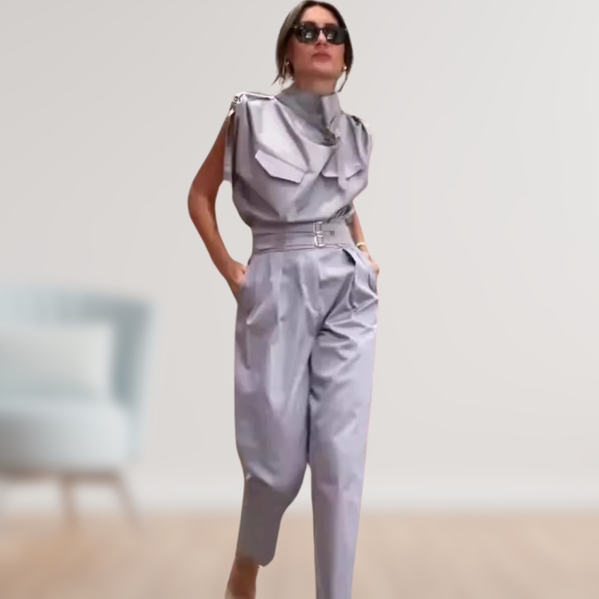 Kvinde i moderne, sølvfarvet jumpsuit med solbriller, poserer i minimalistisk rum. Trendy mode, elegant design, stilfuldt outfit.