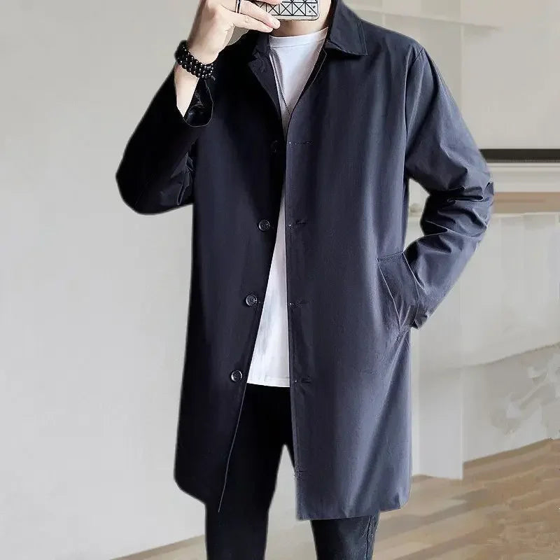 Mand iført stilfuld sort trenchcoat, hvid t-shirt og sorte bukser. Moderne herremode, minimalistisk design, elegant overtøj til efterår og vinter.