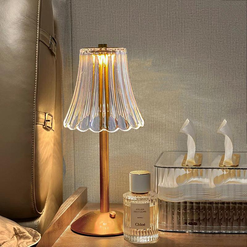 Gennemsigtig glasbordlampe med gylden base ved siden af parfume og servietboks på træbord. Elegant belysning, moderne indretning, hyggelig atmosfære.