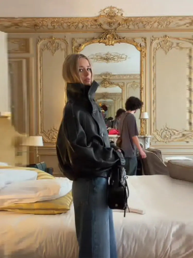 Kvinde i sort jakke og jeans står i elegant, klassisk indrettet værelse med spejl og udsmykkede vægge. Moderne mode, luksusindretning, stilfuldt interiør.