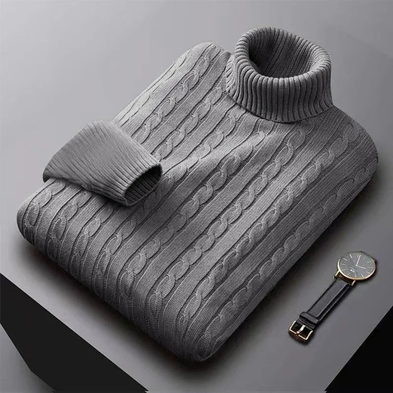 Grå kabelstrikket rullekravesweater på bord ved siden af sort ur. Stilfuld herresweater, vintermode, varm beklædning.