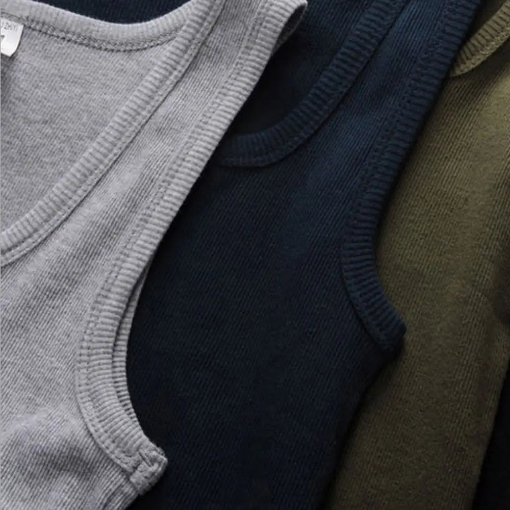 Grå, blå og olivengrønne tanktops i ribstrikstof, stablet. Komfortabelt og stilfuldt tøjvalg til hverdagsbrug.