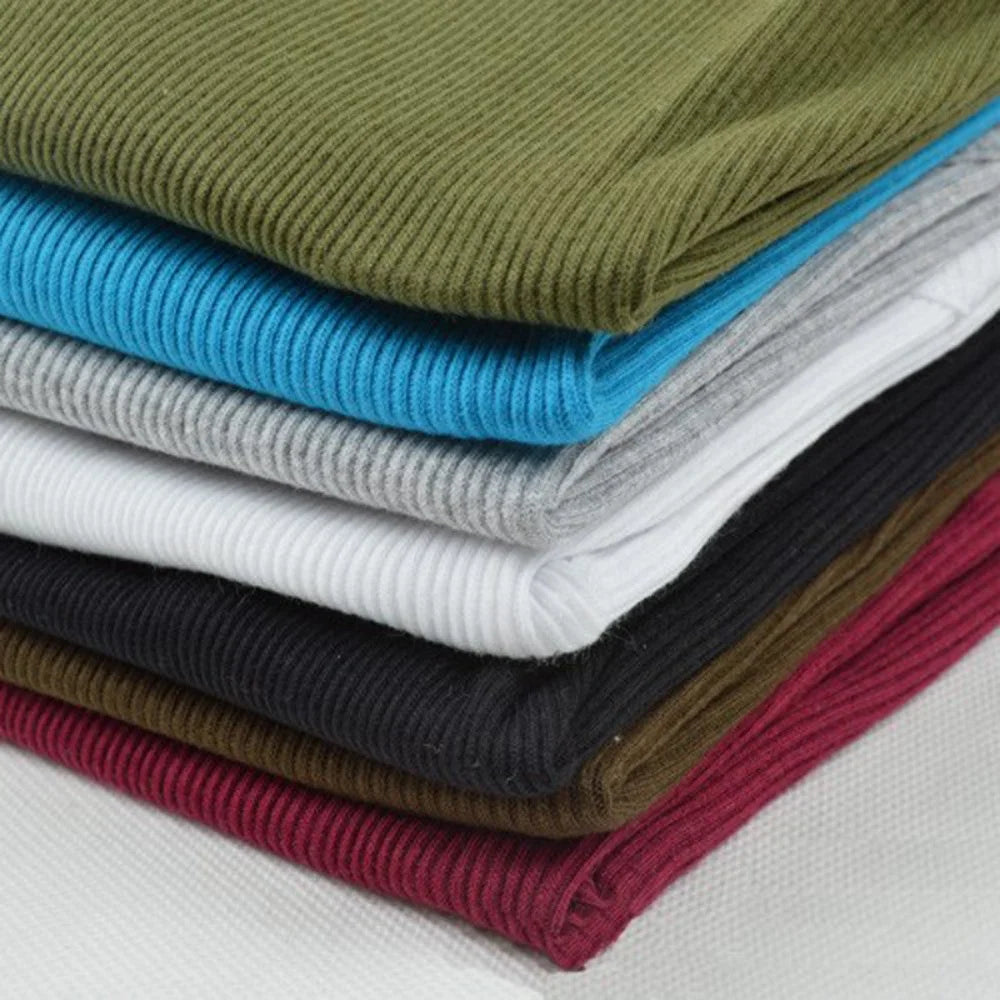 Stabel af farverige ribstrikkede stoffer i forskellige nuancer, herunder grøn, blå, grå, hvid, sort, brun og bordeaux. Perfekt til syning og modeprojekter.