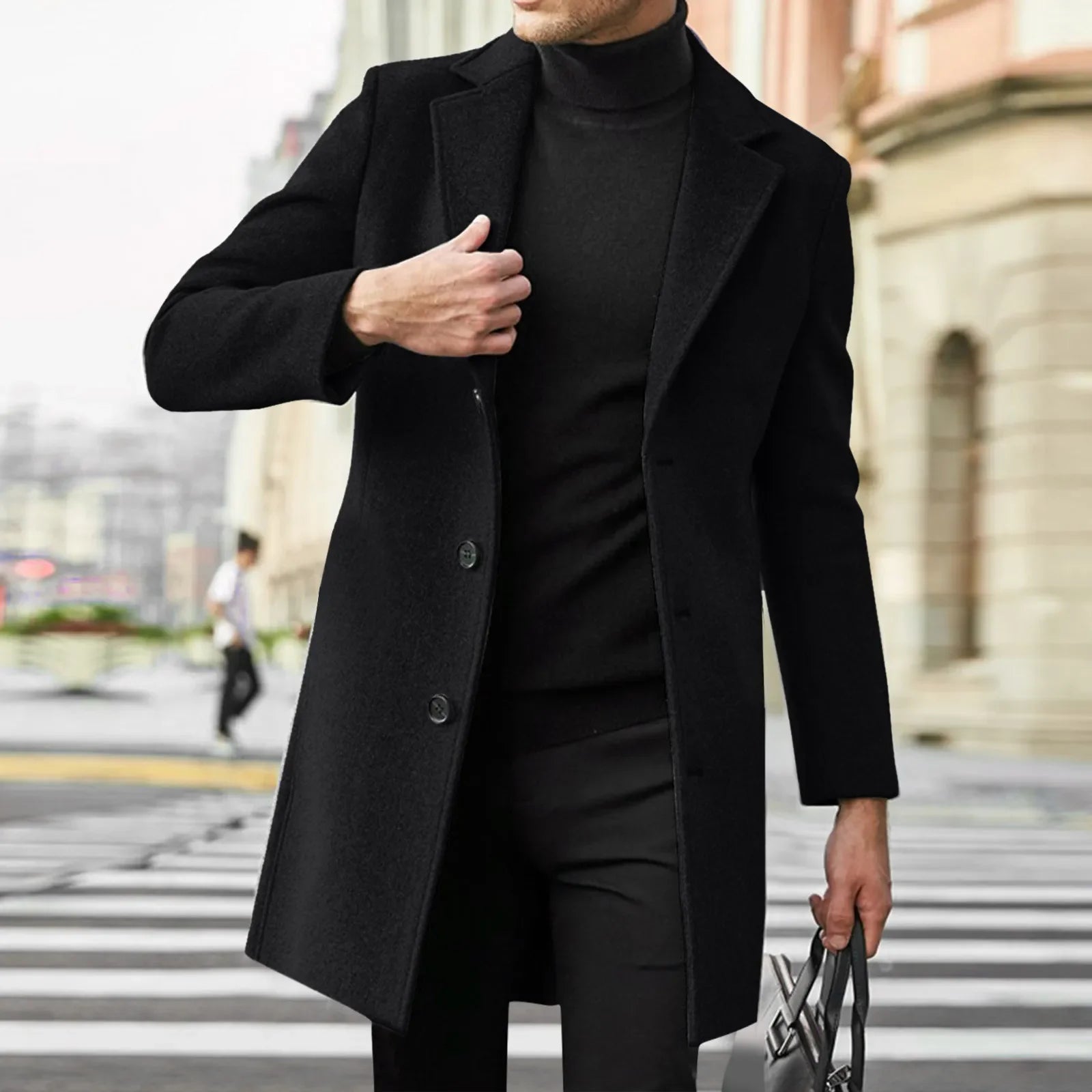 Mand iført sort frakke og turtleneck, krydser gade i bymiljø. Elegant herremode, vintertøj, stilfuldt look, urban baggrund.