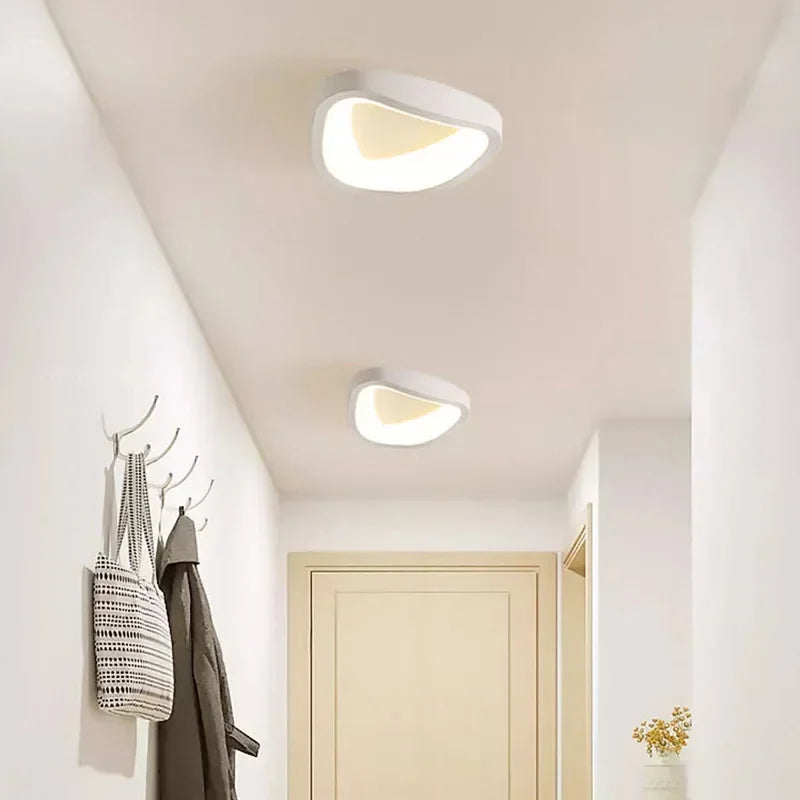 Moderne loftlamper i hvidt design i en lys gang med jakker og tasker på knager. Stilfuld belysning, minimalistisk indretning, skandinavisk stil.