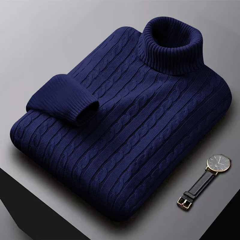 Mørkeblå rullekravesweater i kabelstrik ligger foldet på bord, ved siden af et elegant armbåndsur. Perfekt til vintermode og stil.