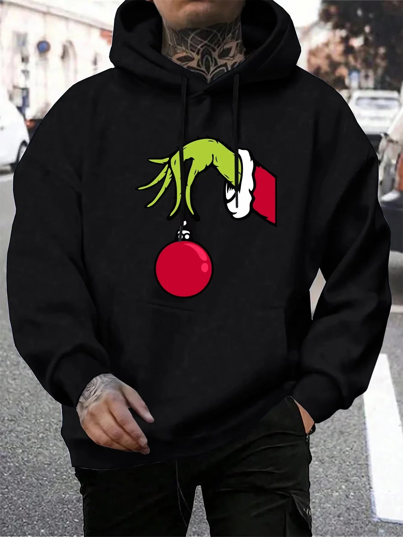 Sort hættetrøje med Grinch-motiv, der holder en rød julekugle. Perfekt til jul, streetwear og vintermode. Unikt design til fans af juleklassikere.