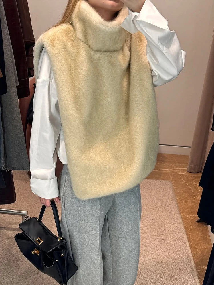 Kvinde iført hvid skjorte og beige pelsvest, grå bukser, holder sort håndtaske. Mode, vintertøj, stilfuldt outfit, shopping.