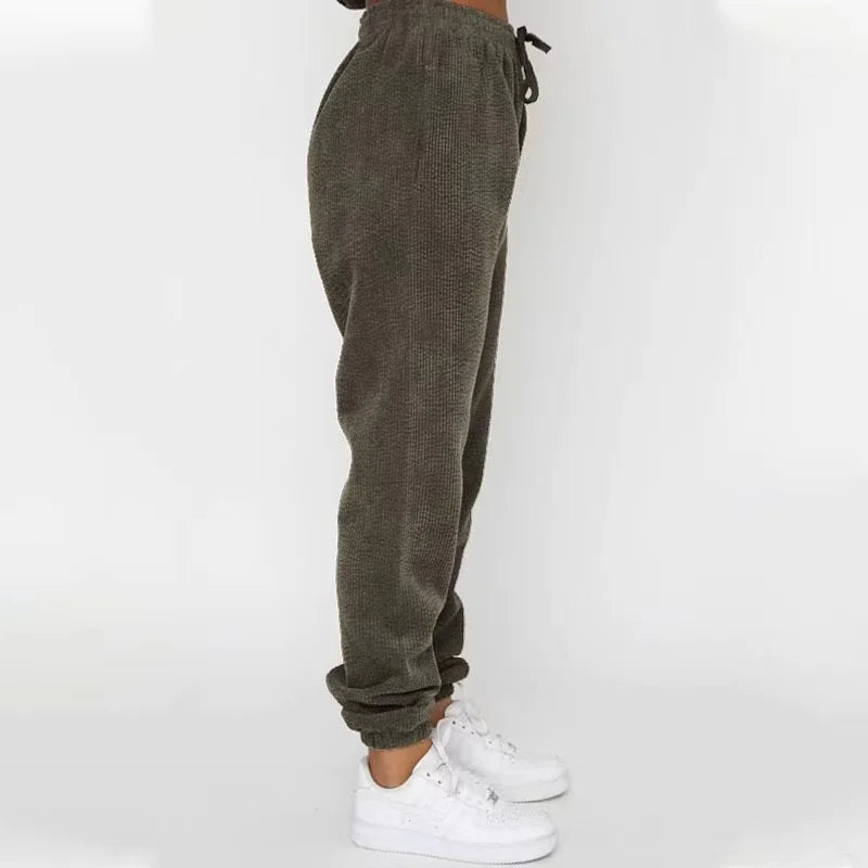 Brune fleece joggingbukser til kvinder, set fra siden, med elastisk talje og manchetter, kombineret med hvide sneakers. Komfortabelt og stilfuldt design.