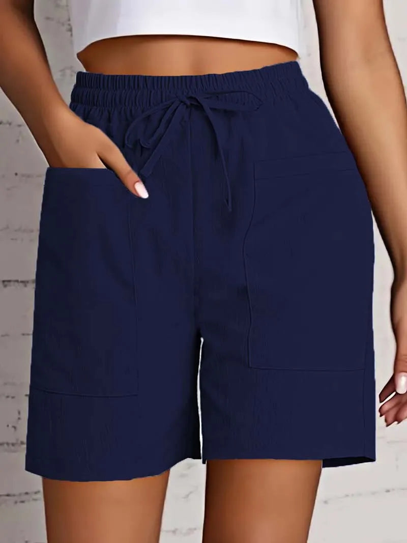 Dame iført mørkeblå shorts med elastisk talje og snøre, to store lommer, mod hvid baggrund. Komfortabelt sommertøj, casual stil.