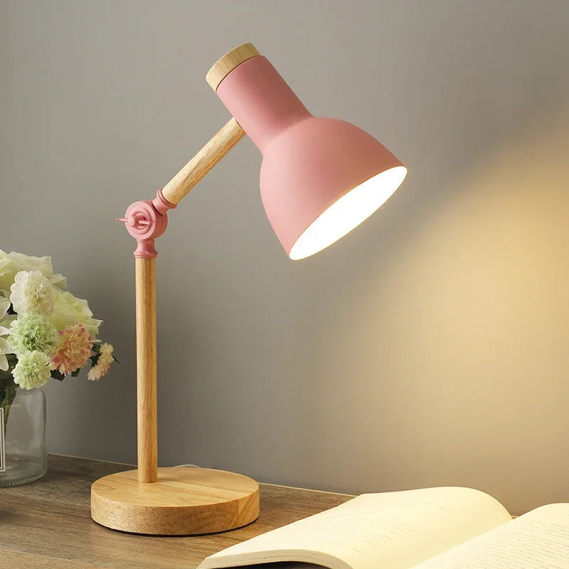 Lyserød bordlampe i træ på skrivebord ved siden af åben bog og blomster, moderne skandinavisk design, belysning til hjemmekontor eller studie.