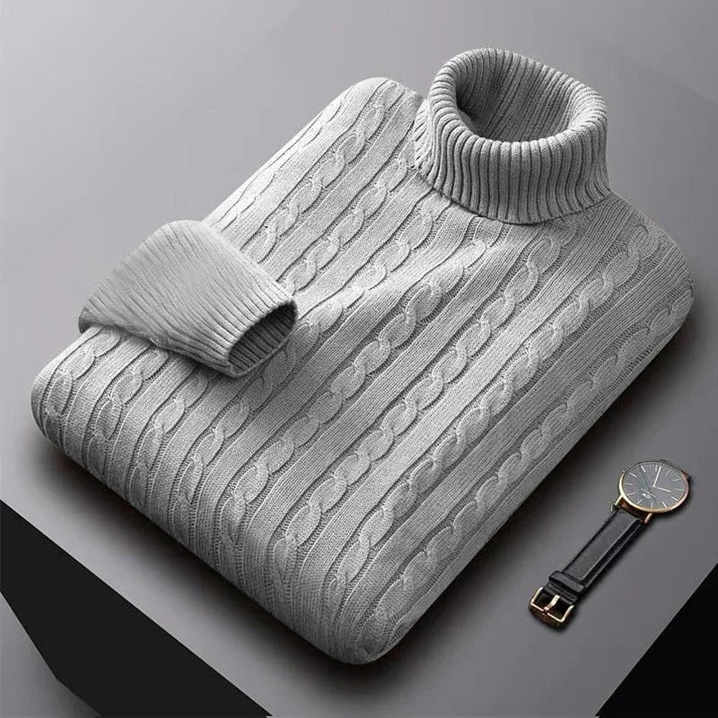Grå kabelstrikket rullekravesweater på bord, ved siden af sort læderrem ur. Stilfuldt vintertøj, moderne herremode, elegant design.