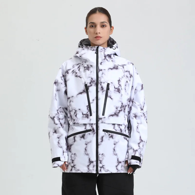 Kvinde iført hvid og sort marmoreret skijakke med hætte, lynlåslommer og sort bukser. Vintertøj, skijakke, mode, udendørsbeklædning.
