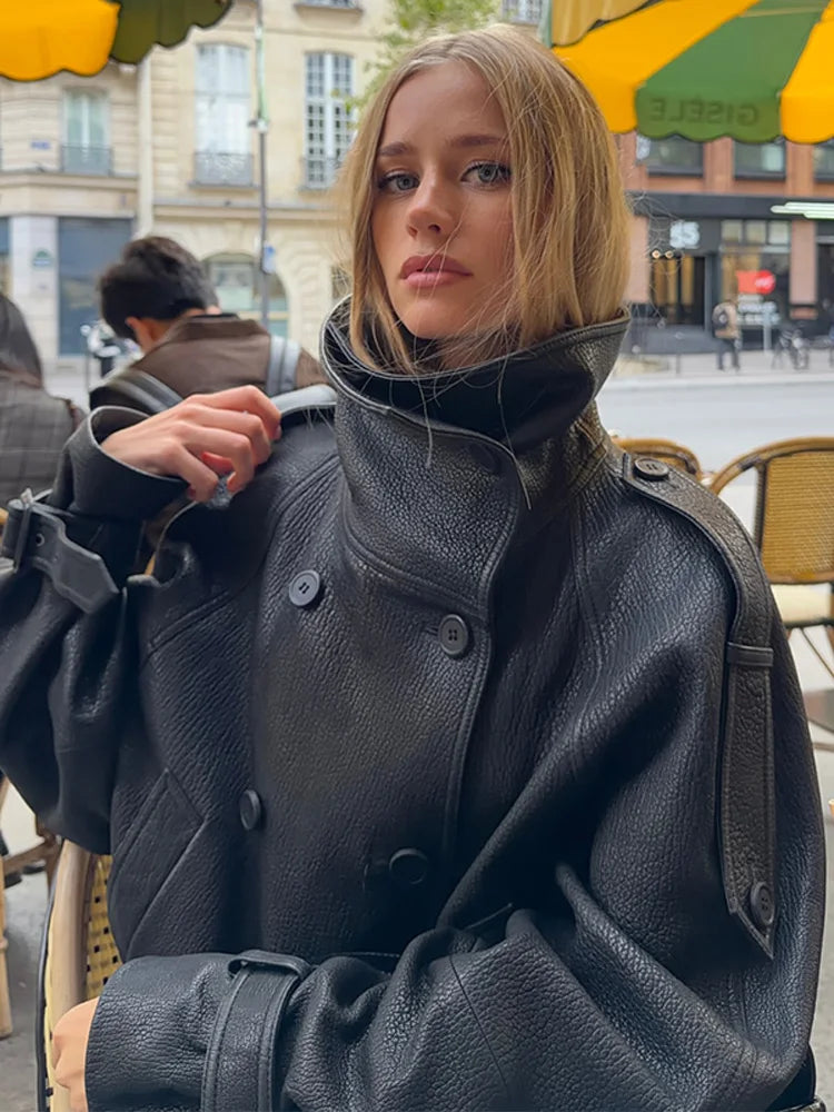 Ung kvinde iført sort læderjakke sidder på café i bymiljø. Mode, street style, efterårstøj, moderne kvindemode, udendørs café.