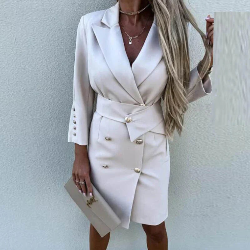 Kvinde i elegant beige blazer-kjole med knapper og bælte, holder en matchende clutch. Perfekt til stilfulde forretnings- eller aftenbegivenheder.