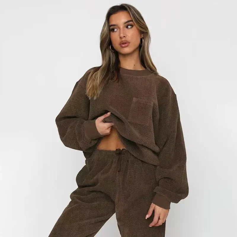 Kvinde iført brun, behagelig loungewear-sæt med langærmet trøje og bukser. Perfekt til afslapning og hjemmetøj. Trendy og stilfuldt design.
