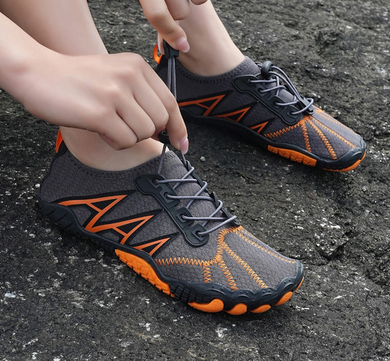 Person snører grå og orange løbesko på asfalt. Minimalistiske, letvægtsdesign, ideelle til udendørs sport og løb. Komfortable og åndbare materialer.
