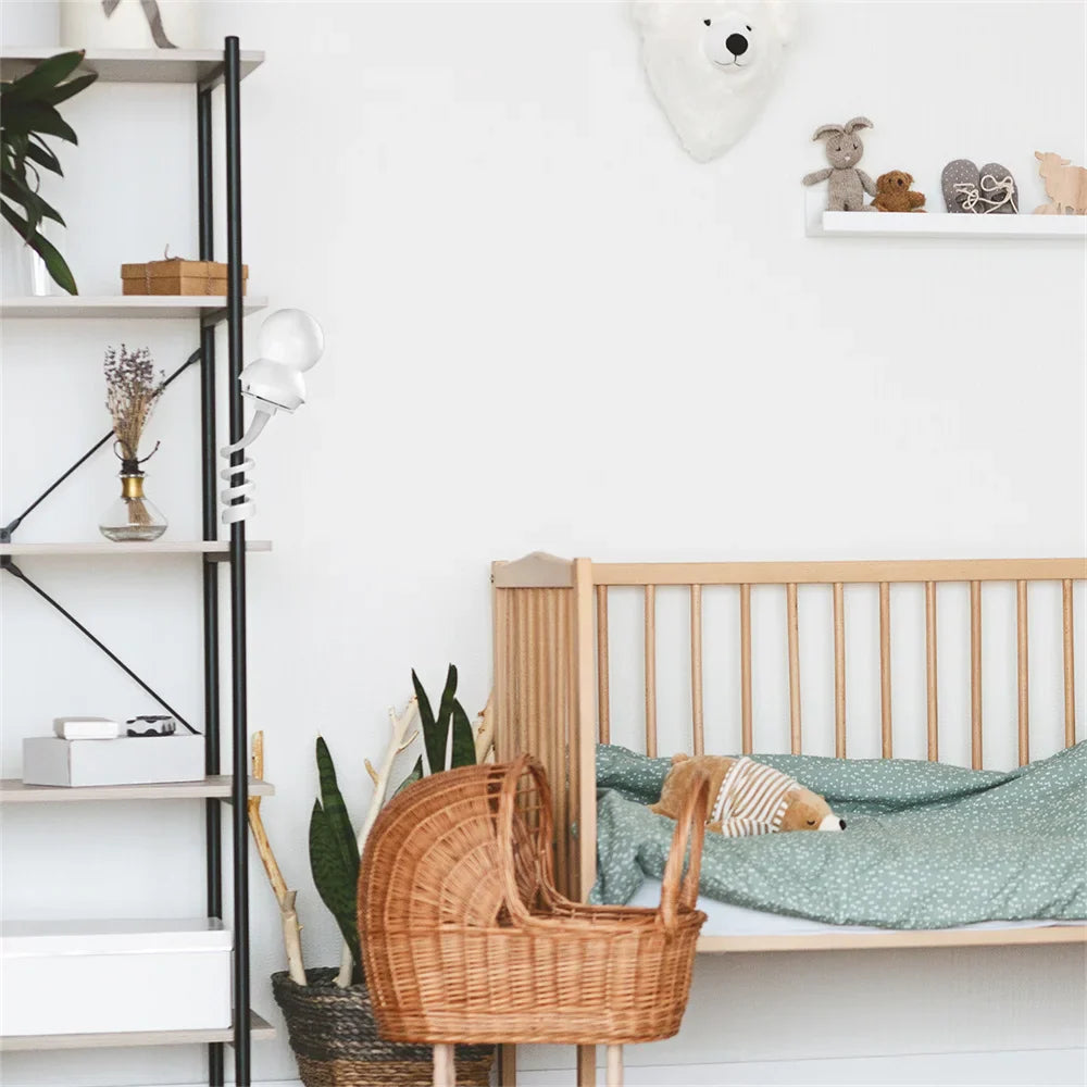 Lyst børneværelse med tremmeseng, grøn dyne, flettet vugge, hylde med bamser og planter. Skandinavisk indretning, minimalistisk design.