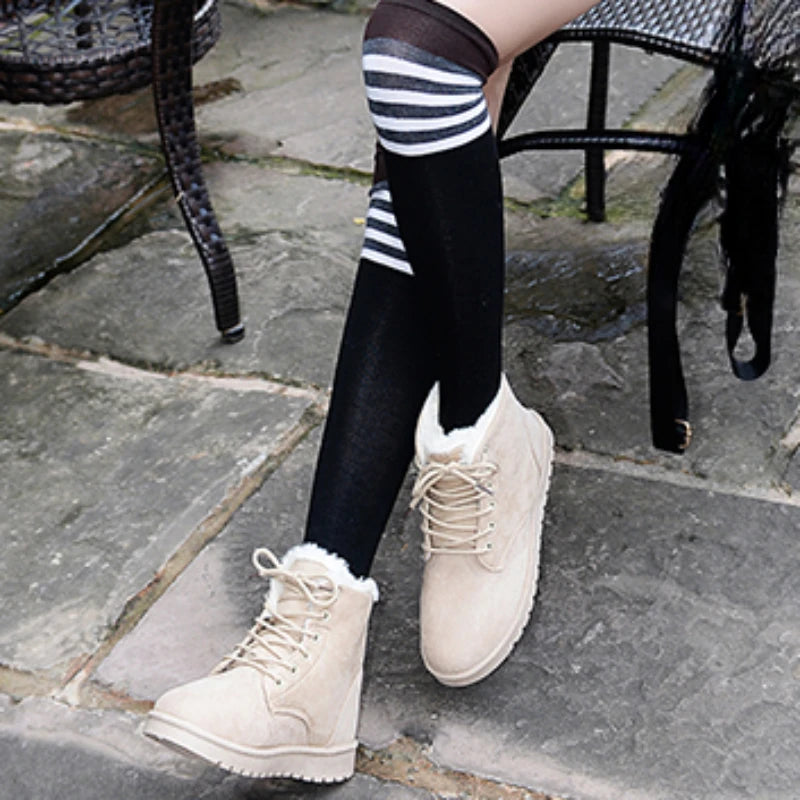 Beige vinterstøvler med pelsfor, sorte knæstrømper med striber, kvinde sidder på stol udendørs. Komfortable, stilfulde sko til koldt vejr.