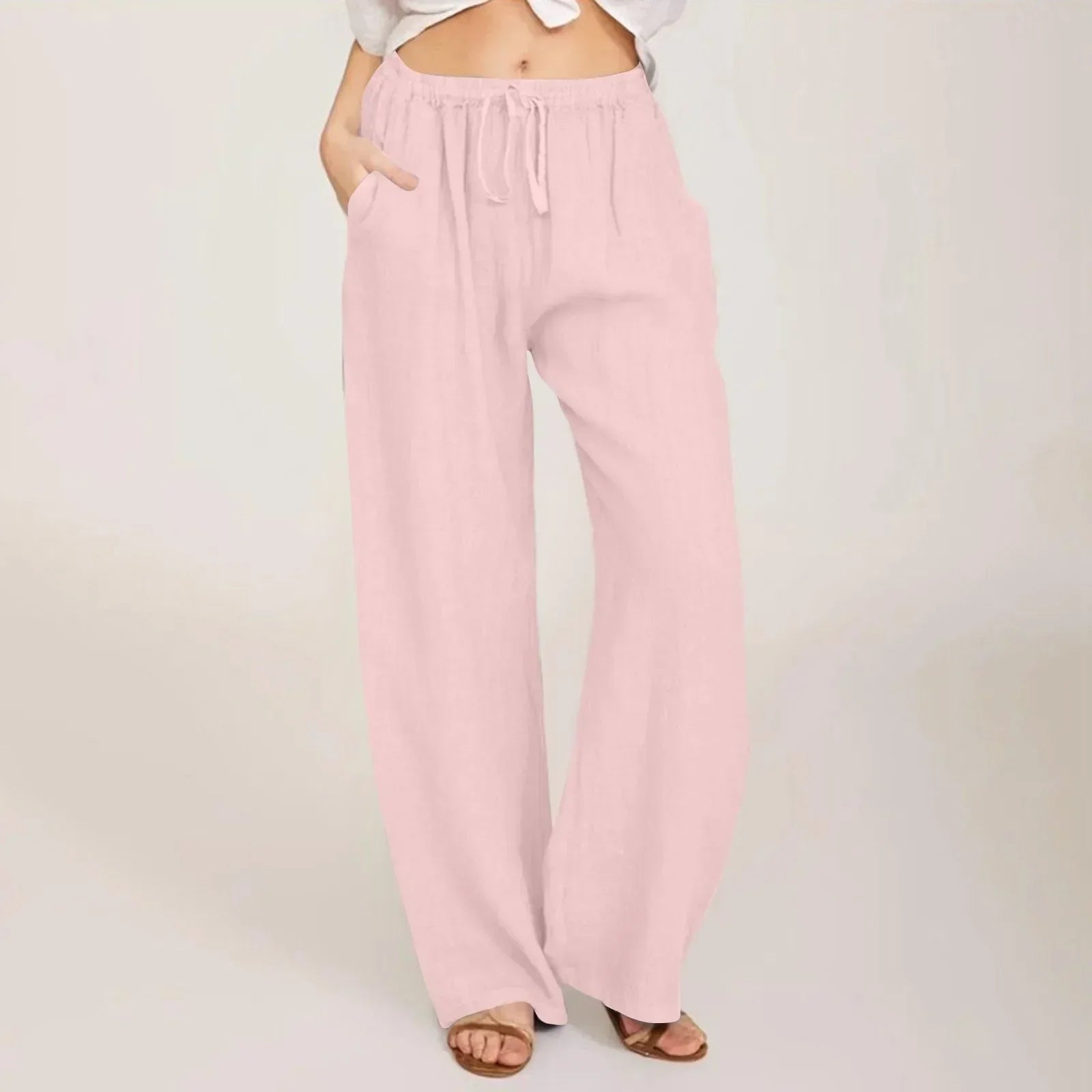 Kvinde iført lyserøde, løstsiddende bukser med snøre og lommer, kombineret med en hvid top. Perfekt til afslappet sommermode og komfort.