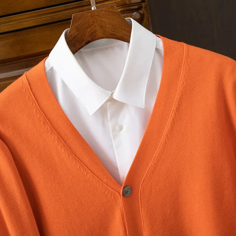 Orange cardigan med V-udskæring over en hvid skjorte på en træbøjle. Stilfuldt og moderne tøj til efterår og vinter.