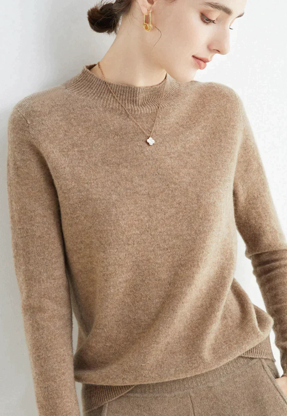 Kvinde iført beige cashmere sweater, elegant design, minimalistisk stil, gyldne øreringe, afslappet mode, luksuriøst tøj, efterårslook.