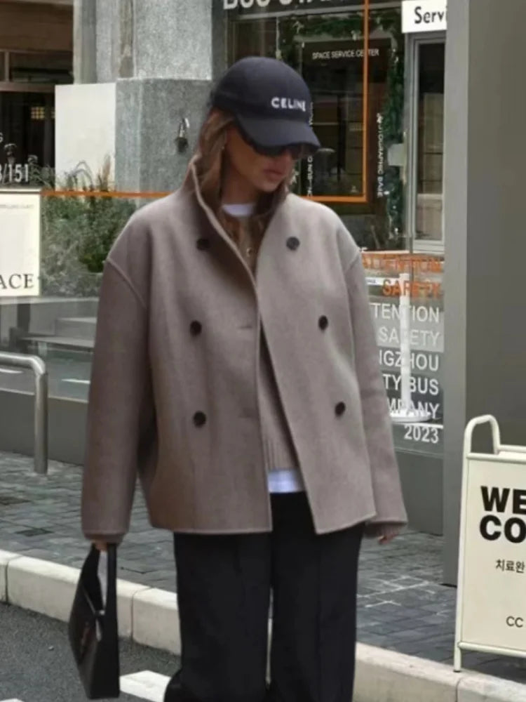 Kvinde iført beige frakke og sort Celine kasket, står på gaden. Mode, efterårstøj, street style, moderne look, bymiljø.