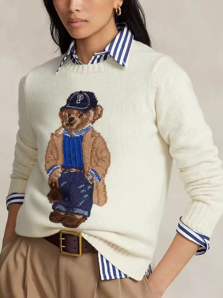 Kvinde iført hvid sweater med bjørnemotiv, blå stribet skjorte og beige bukser. Mode, efterårstøj, casual stil, trendy look.