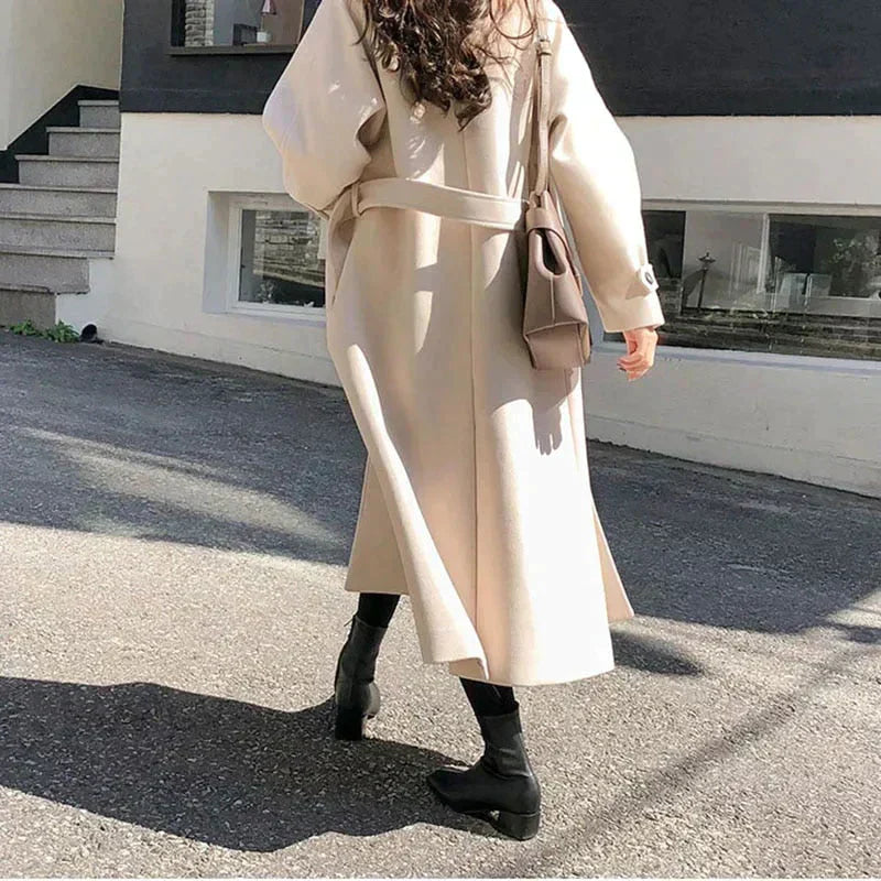 Kvinde iført lang beige frakke og sorte støvler går på gaden. Elegant mode, efterårsjakke, stilfuldt outfit, byliv.