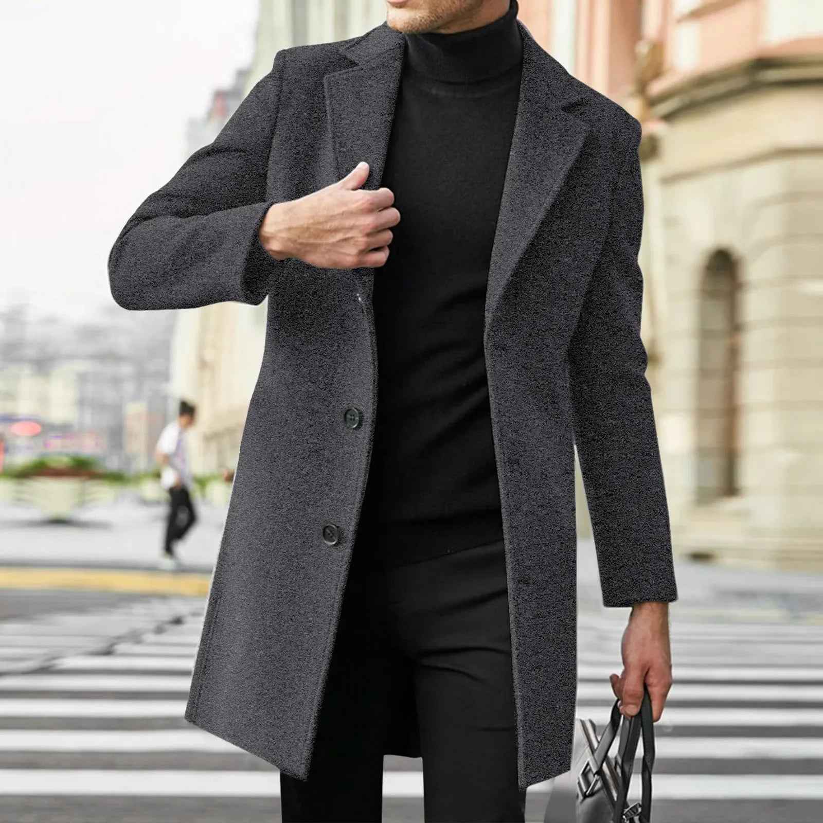 Mand iført grå frakke og sort turtleneck, går på byens gade med bygninger i baggrunden. Elegant herremode, vinterfrakke, stilfuldt look.
