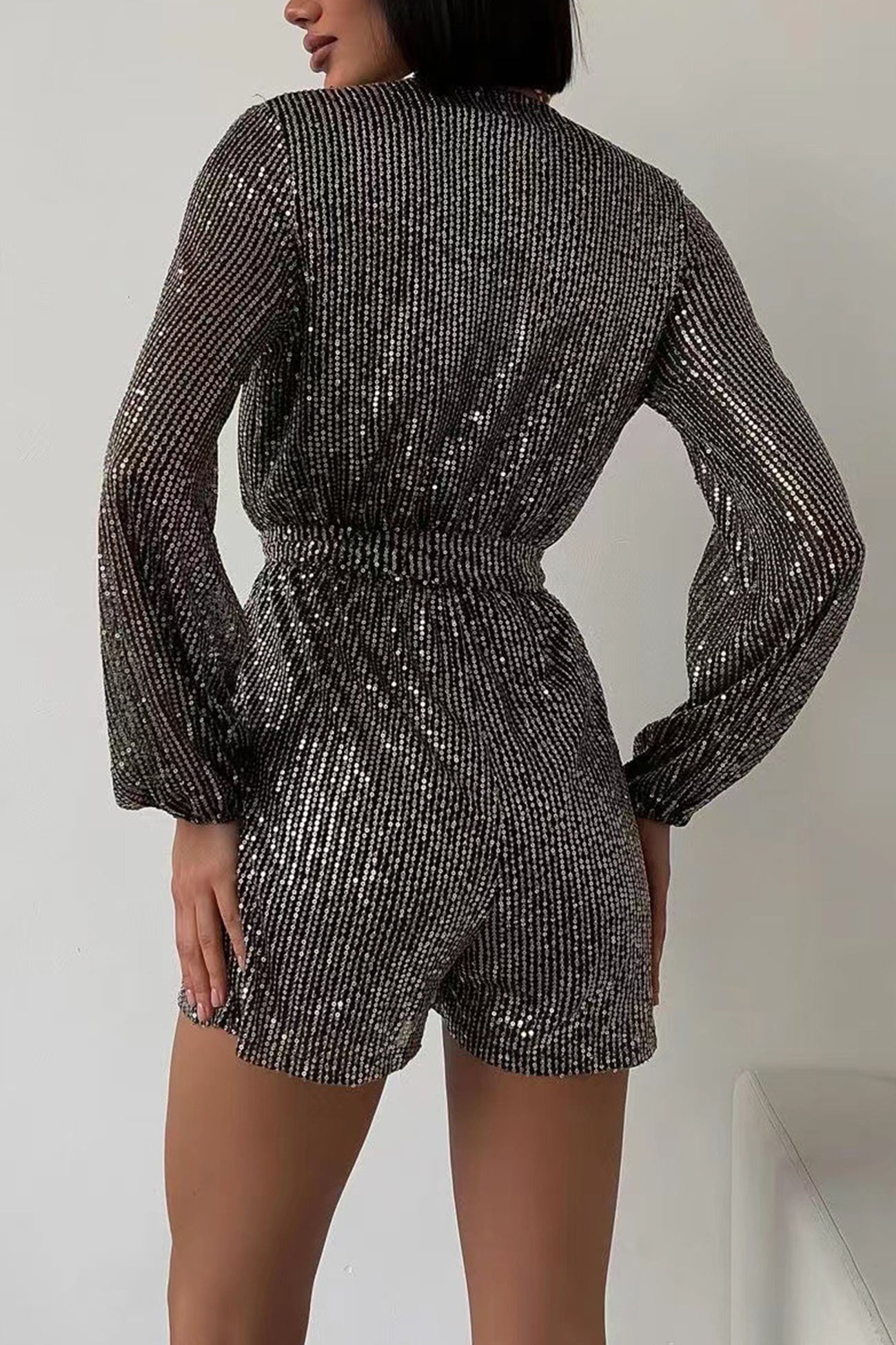Kvinde iført sort glitrende jumpsuit med lange ærmer, set bagfra. Elegant festtøj, perfekt til aftenbegivenheder og modebevidste kvinder.