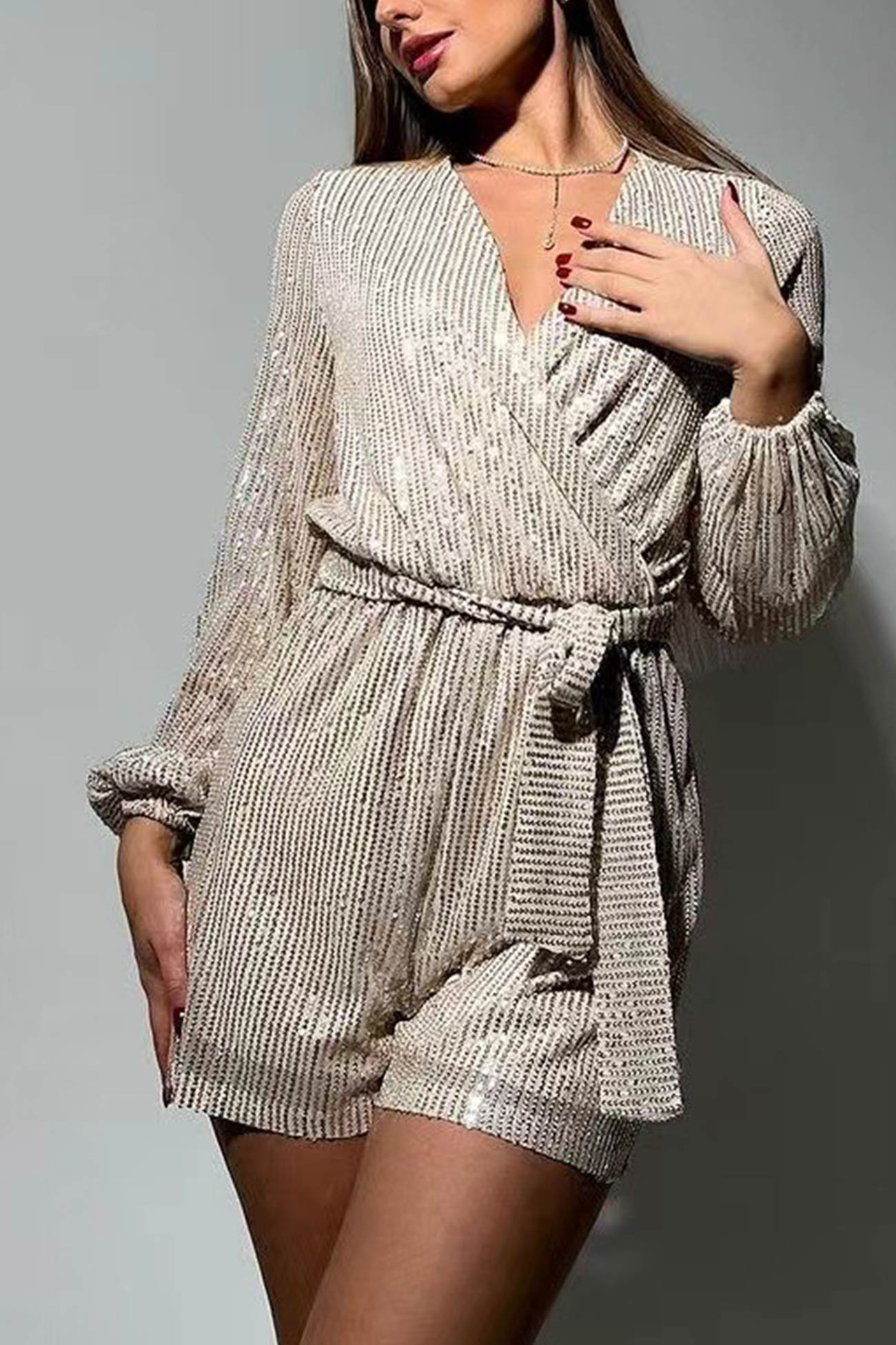 Kvinde iført glitrende, beige jumpsuit med lange ærmer og bælte, elegant design, perfekt til festlige lejligheder.