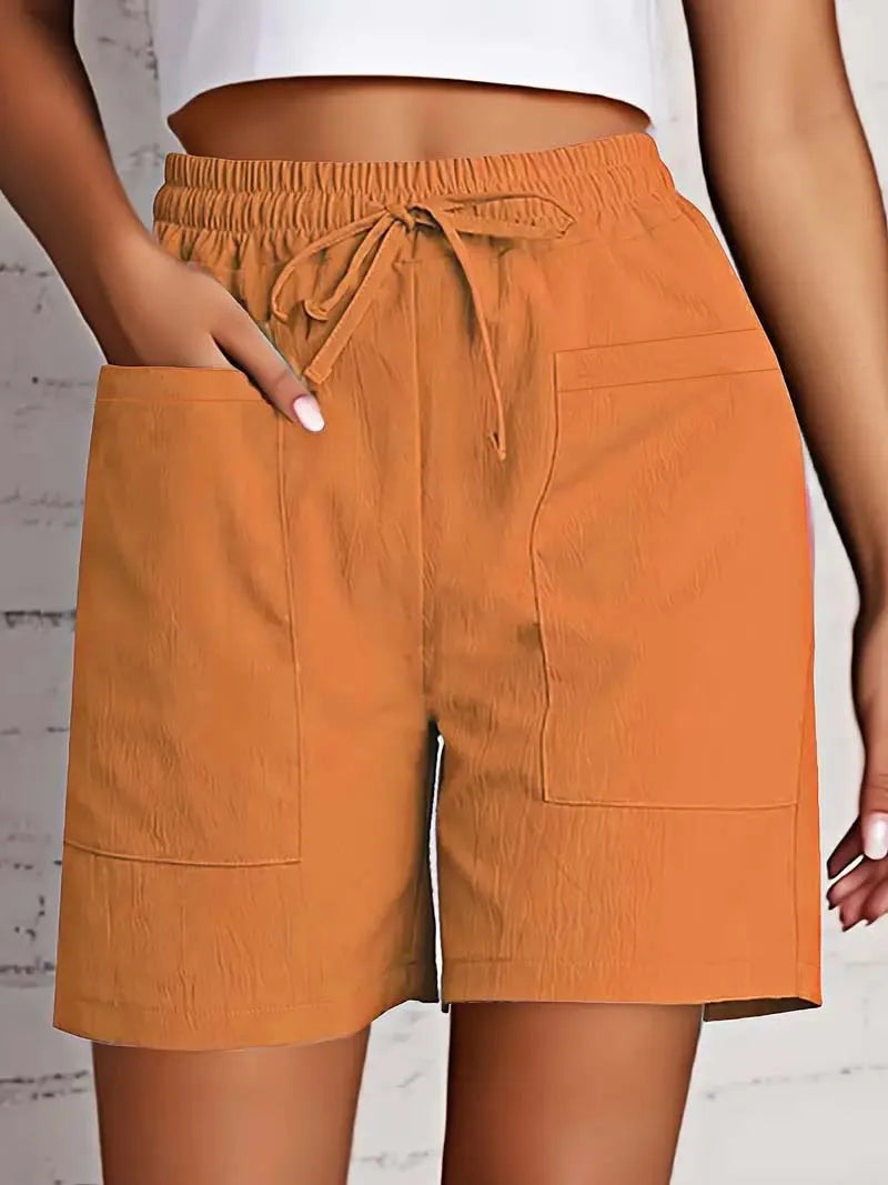 Kvinde iført orange shorts med elastisk talje og snøre, to store forlommer, mod hvid baggrund. Sommermode, behagelige shorts til kvinder.