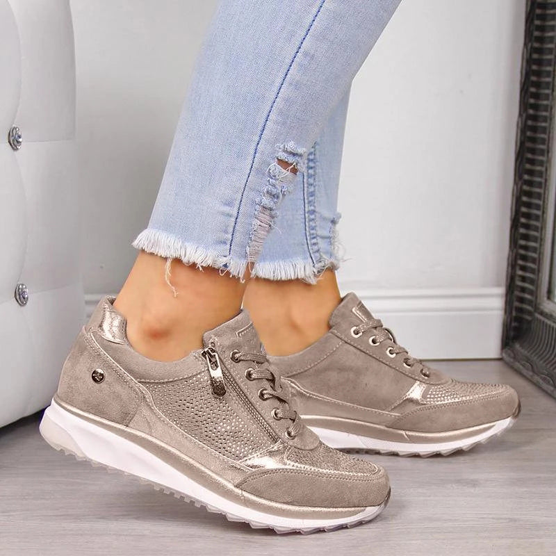 Beige sneakers til kvinder med hvid sål, perforeret design og lynlåsdetalje. Kombineret med lyseblå, slidte jeans. Moderne og stilfuldt fodtøj.