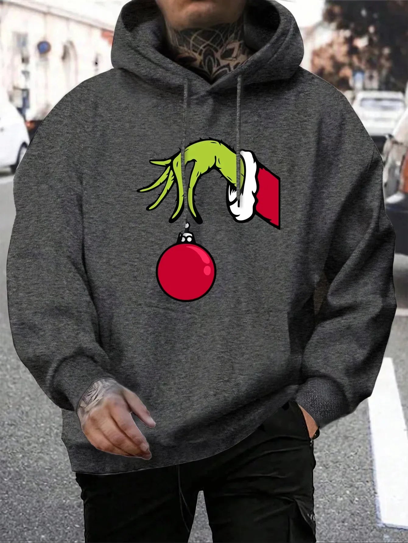 Grå hættetrøje med Grinch-motiv, der holder en rød julekugle. Perfekt til jul, unisex streetwear, komfortabel og stilfuld vintermode.