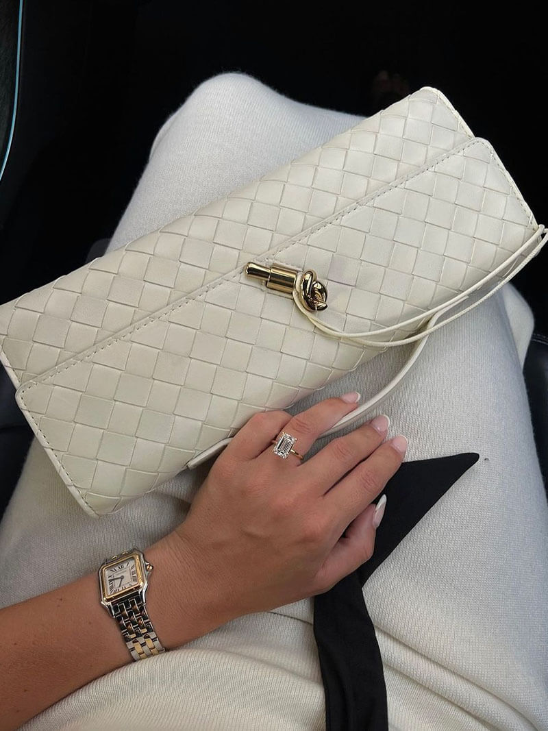 Hvid flettet clutch taske med guldlås, kvinde med diamant ring og ur, elegant mode tilbehør, luksus stil, håndtaske på hvidt tøj.