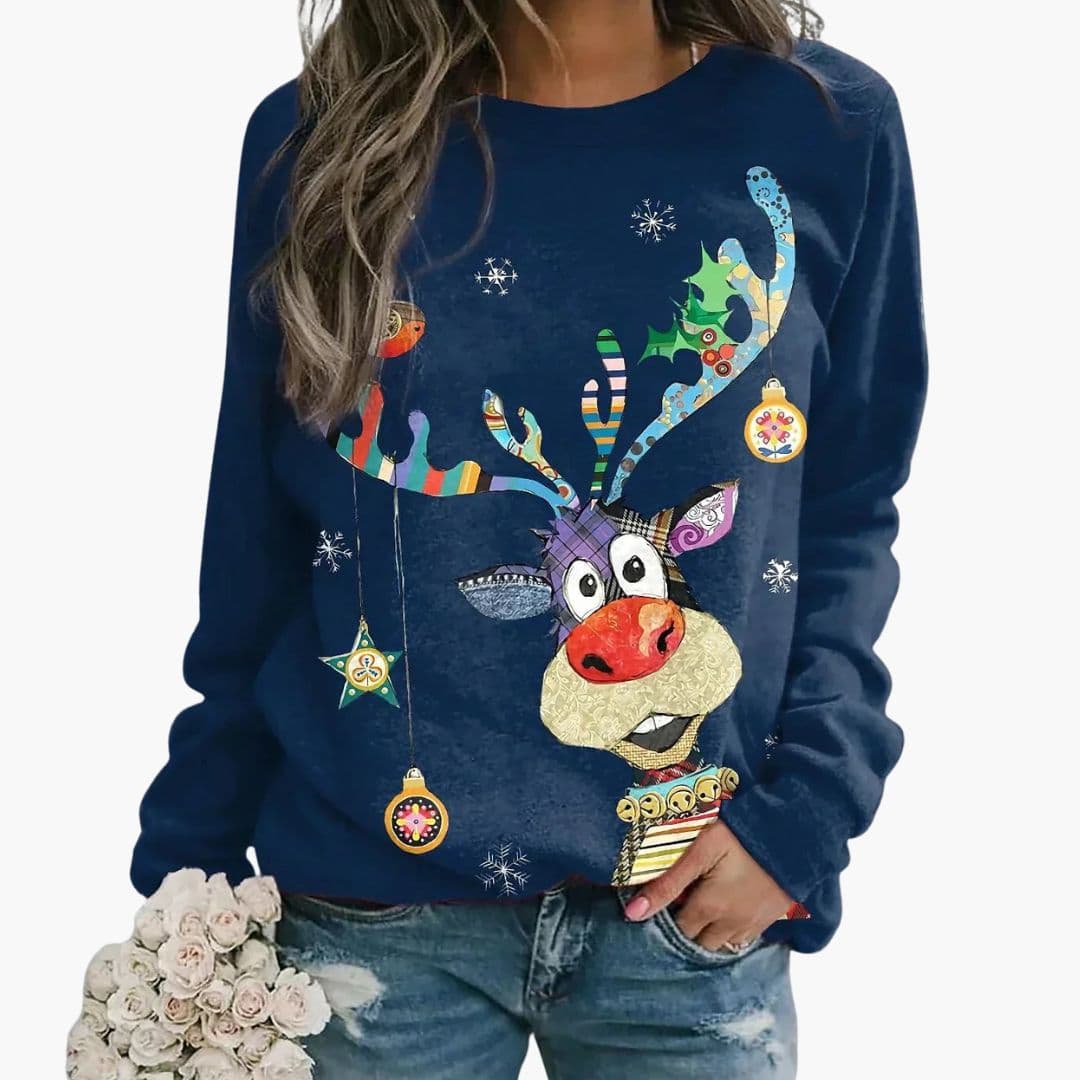 Kvinde iført blå juletrøje med farverig rensdyrgrafik og snefnug, holder en buket hvide blomster. Festlig vintermode, casual look.