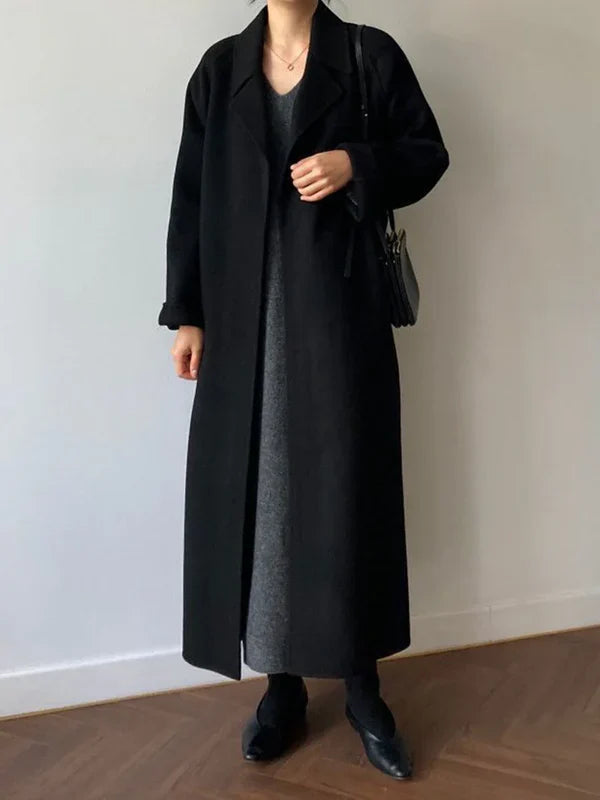 Sort frakke dame, lang uldfrakke, minimalistisk design, grå kjole, sort taske, stilfuldt vinteroutfit, moderne kvindemode, elegant look.