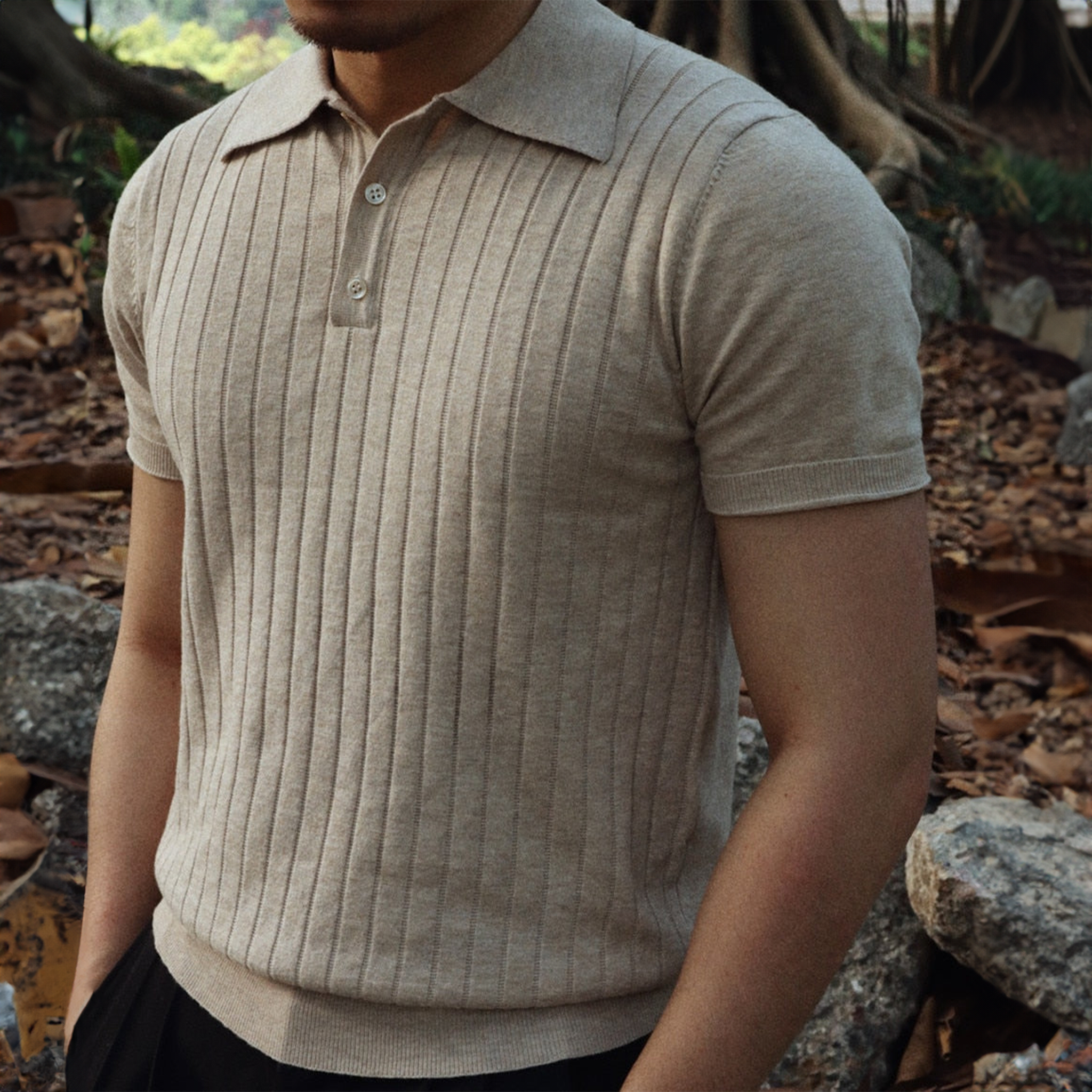 Mand iført beige striktrøje med korte ærmer i naturmiljø. Stilfuld herremode, ribstrikket design, efterårslook, casual elegance.