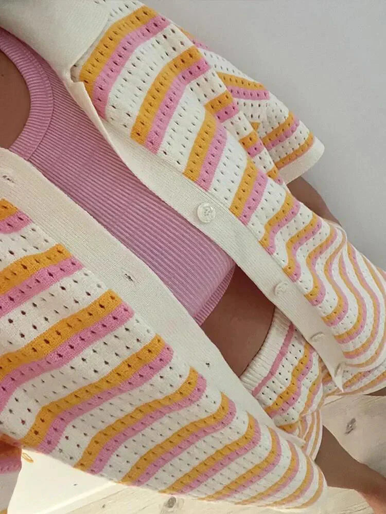 Kvinde iført strikket cardigan og shorts med lyserøde, gule og hvide striber, kombineret med en lyserød top. Farverigt sommertøj, strikmode.