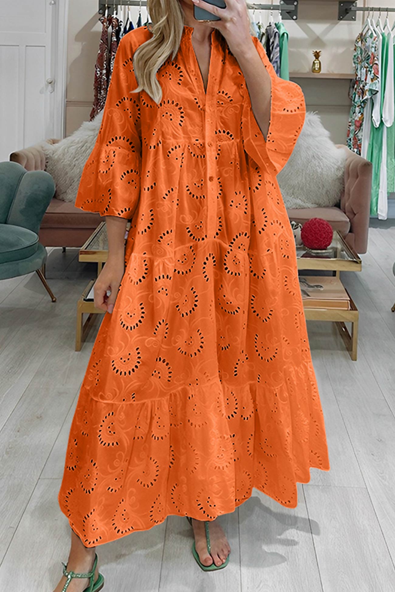Kvinde iført lang orange kjole med broderi, stående i moderne stue. Sommermode, boheme-stil, farverig kjole, trendy tøj.