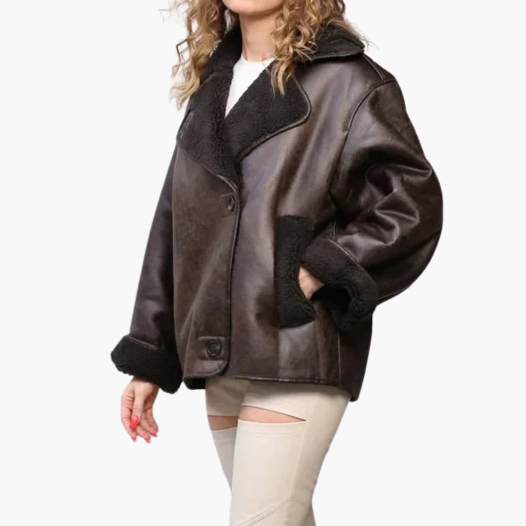 Kvinde iført brun læderjakke med sort pelsfor, store kraver og lommer. Trendy vintermode, stilfuld overtøj, moderne design.