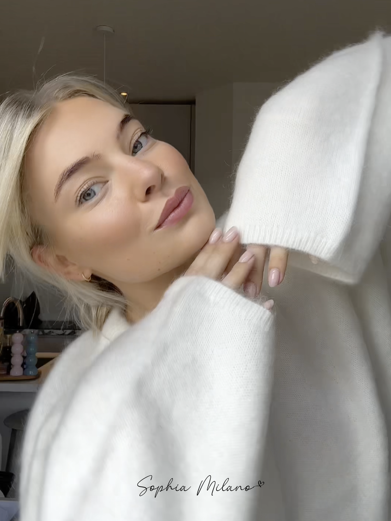 Jeg ved ikke, hvem personen er, men her er en beskrivelse: Kvinde i hvid sweater poserer indendørs, naturligt lys, afslappet stil, moderne mode, skandinavisk design.