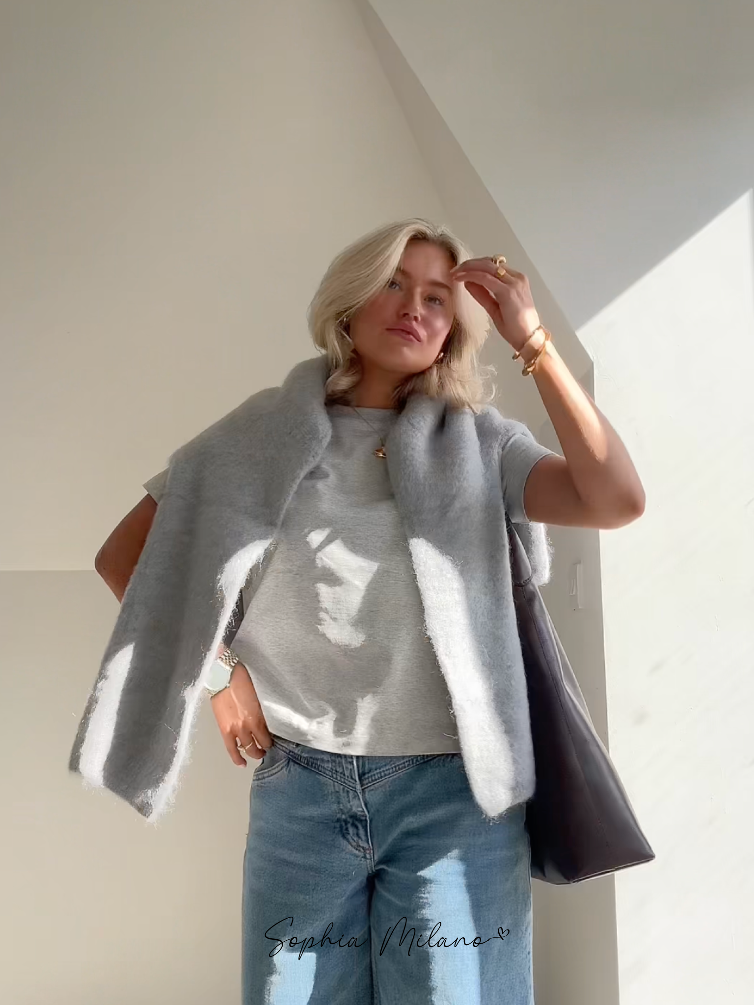 Ung kvinde i grå t-shirt og jeans, med grå sweater over skuldrene, poserer i sollys. Moderne mode, afslappet stil, skandinavisk design.