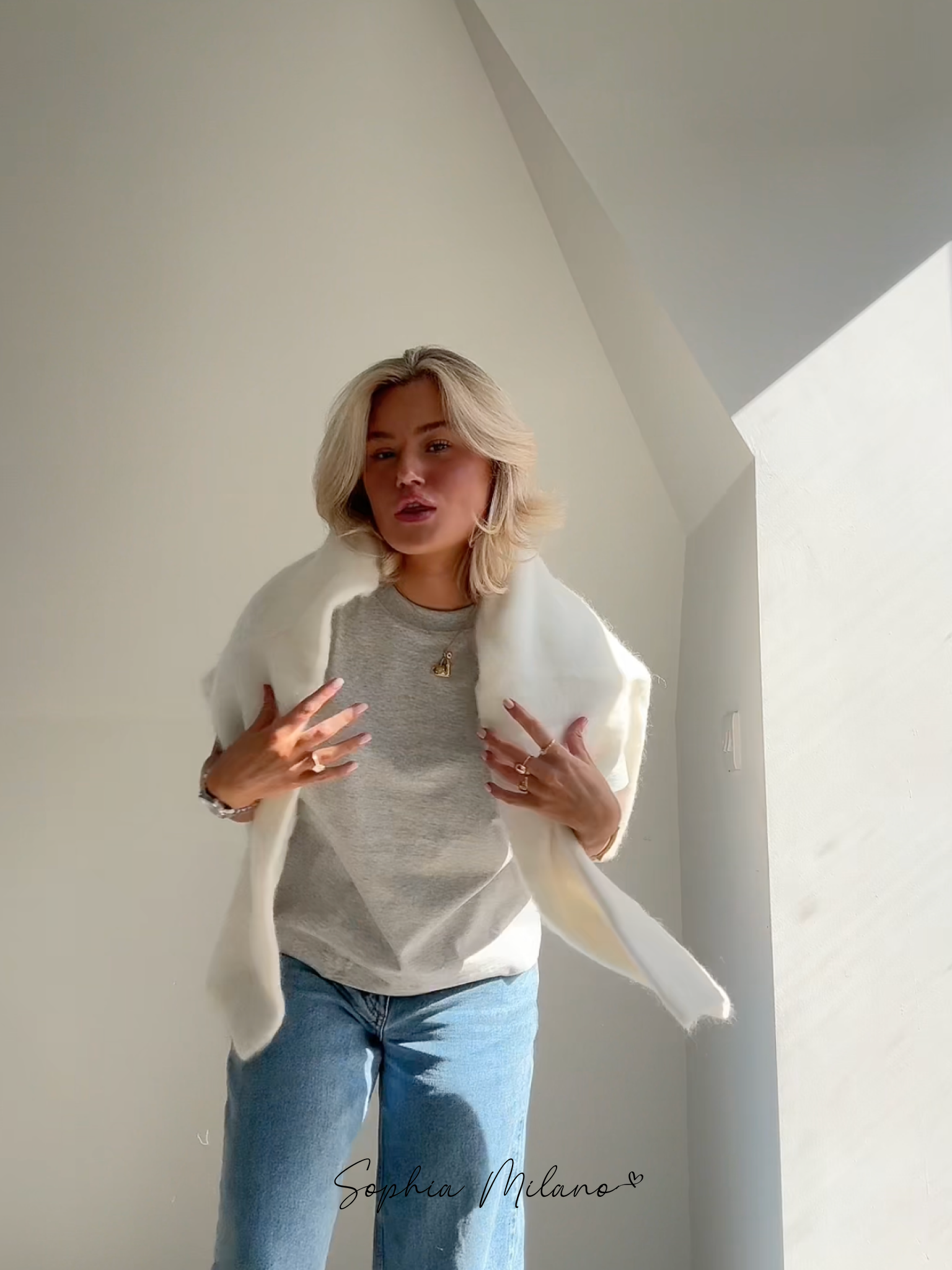 Ung kvinde i grå t-shirt og jeans med hvid pelsjakke, poserer i naturligt lys. Moderne mode, minimalistisk stil, skandinavisk indretning.