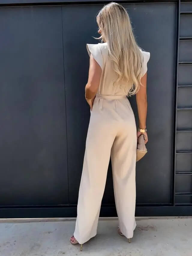 Langhåret kvinde i beige buksedragt står med ryggen til foran sort væg. Elegant mode, moderne stil, sommeroutfit, kvindetøj.