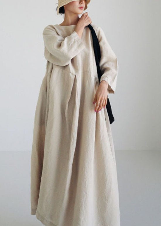 Kvinde i lang, beige kjole og hat, minimalistisk mode, skandinavisk stil, bæredygtigt tøj, moderne design, enkel elegance, neutral farvepalet.