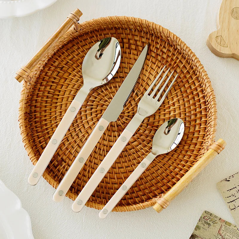 Flettet kurv med bestik: ske, kniv, gaffel og teske med hvide håndtag. Perfekt til borddækning og køkkenindretning.