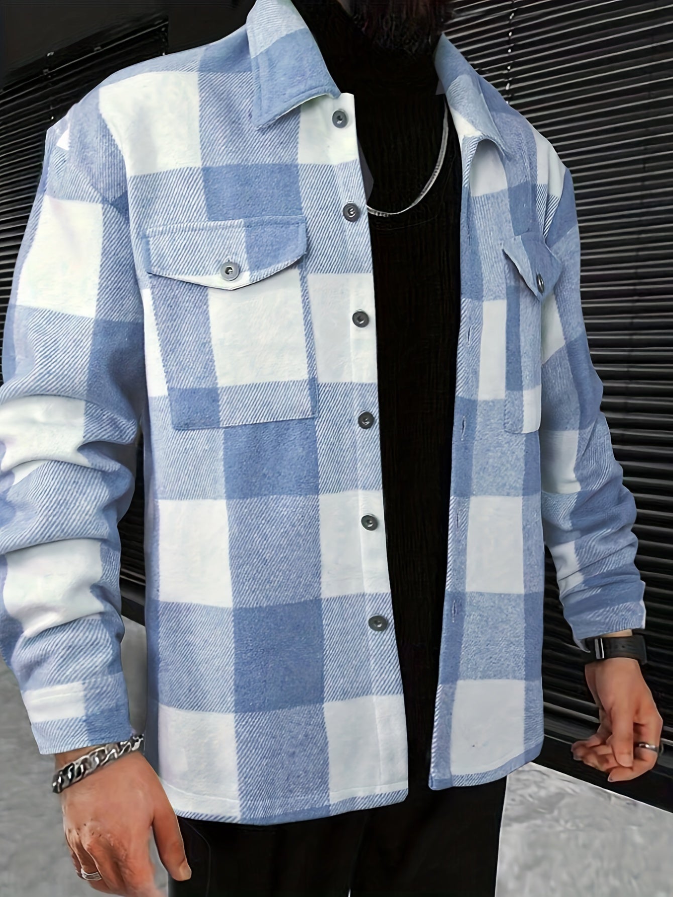 Mand iført blå-hvid ternet skjortejakke, sorte bukser og sort trøje. Skjorten har knapper og brystlommer. Mode, herretøj, stil.
